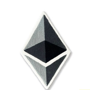 May include: A black and white geometric design in the shape of a diamond. The design is made of a soft, textured material, possibly fabric or rug.