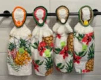 May include: Four white kitchen towels with a pineapple and tropical leaf design. Each towel has a pineapple-shaped holder with a colorful floral design.