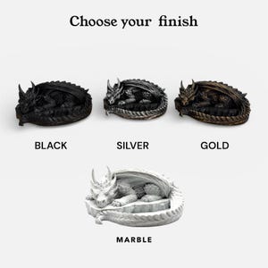 A product option guide titled "Choose your finish" for the Nap Twenty dragon dice holder. The image showcases four different 3D-printed finishes: a matte Black, a metallic Silver, a weathered Gold, and a light speckled Marble. Each sleeping dragon model is labeled with its respective color name, demonstrating the variety of styles available for D&D players.