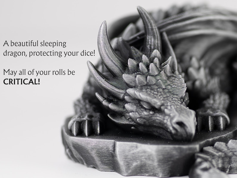 An extreme close-up of the sleeping dragon's head, highlighting the fine 3D-printed textures of its scales and horns in a metallic finish. To the left, stylized text reads: "A beautiful sleeping dragon, protecting your dice! May all of your rolls be CRITICAL!" The focus is tight on the dragon's peaceful face, conveying a sense of quality and craftsmanship.