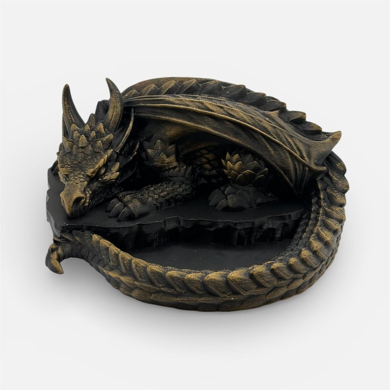 A top-down, angled view of the "Nap Twenty" 3D-printed dragon dice holder in an antique gold finish. The sleeping dragon is coiled into a circle, with its head resting near its tail, creating a central basin for dice. The metallic gold filament highlights the intricate scale textures and spinal ridges, giving it a weathered, treasure-like appearance against a plain white background.