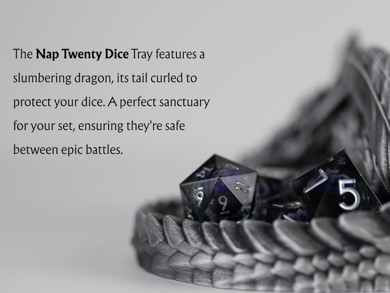 A close-up, artistic shot of the Nap Twenty Dice Tray showing galaxy-themed dice resting within the protective curve of a 3D-printed dragon's tail. Descriptive text on the left reads: "The Nap Twenty Dice Tray features a slumbering dragon, its tail curled to protect your dice. A perfect sanctuary for your set, ensuring they're safe between epic battles." The focus is sharp on the metallic scale texture and the shimmering dice.