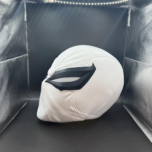 以下が含まれることがあります： 黒いアイマスクが付いた白いヘルメット。ヘルメットはテクスチャ加工された表面を持ち、リングライトで照らされています。アイマスクはメッシュデザインです。