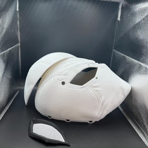 以下が含まれることがあります： 目の開口部と別々のアイピースを備えた、白くテクスチャ加工されたマスク。マスクは湾曲したデザインで、耐久性のある素材で作られている可能性があります。アイピースは、白いメッシュが付いた黒色です。