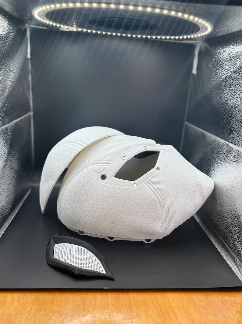 以下が含まれることがあります： 目の開口部と別々のアイピースを備えた、白くテクスチャ加工されたマスク。マスクは湾曲したデザインで、耐久性のある素材で作られている可能性があります。アイピースは、白いメッシュが付いた黒色です。