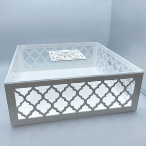 May include: A clear acrylic box with a white, geometric, openwork design on the sides. The box has a lid with a small, decorative, white square in the center. The box is designed to hold items.