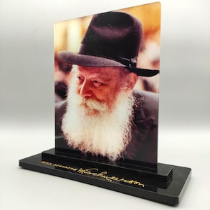 May include: A portrait of a man with a long white beard and a black hat, displayed on a black rectangular base. The base has gold text that reads "With blessing M. Schneerson". The image is a vertical rectangle.