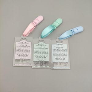 May include: Three clear plastic cards with Hebrew text and a prayer on each card. Each card has a different coloured plastic clip attached to the top. The clips are pink, light blue and green.