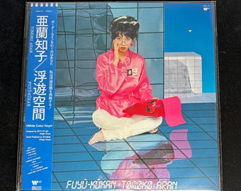 Può includere: Un album in vinile intitolato "FUYU-KUKAN" di Tomoko Aran. La copertina dell'album presenta una donna in abito rosa, seduta di fronte a uno sfondo geometrico. Il titolo dell'album e il nome dell'artista sono in giapponese e inglese.
