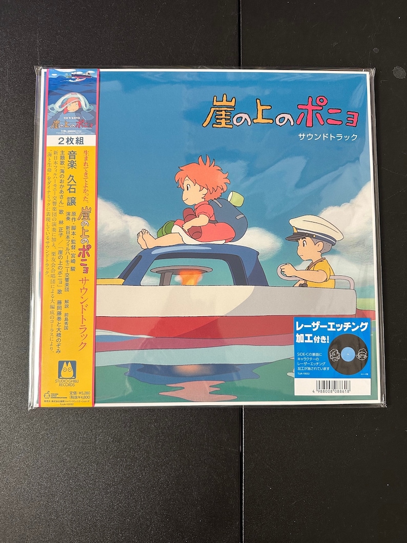 May include: A blue and white vinyl record cover featuring a picture of a girl and a boy on a boat. The title of the record is "崖の上のポニョ" (Gake no Ue no Ponyo) and the text "サウンドトラック" (Sound Track) is below the title. The record is a 2-disc set and features music by Joe Hisaishi.