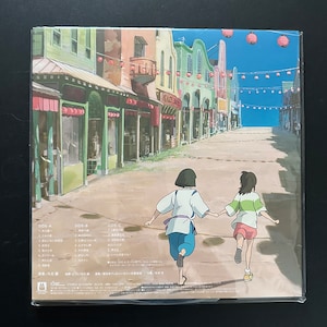 May include: A vinyl record featuring a colorful illustration of a street scene with two animated figures running. The artwork depicts a vibrant town with buildings in various colors, red lanterns, and text in Japanese. The record is sealed in plastic.