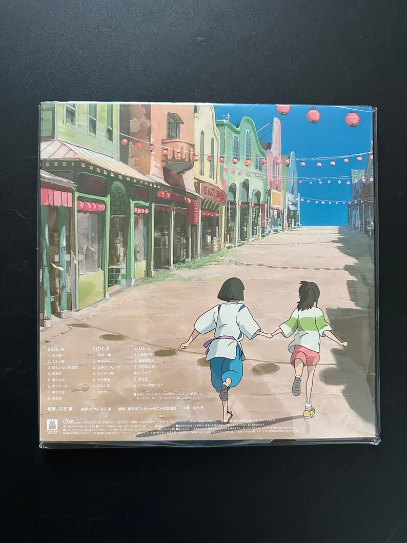 May include: A vinyl record featuring a colorful illustration of a street scene with two animated figures running. The artwork depicts a vibrant town with buildings in various colors, red lanterns, and text in Japanese. The record is sealed in plastic.