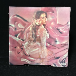 May include: A pink album cover featuring a woman with a flower in her hair, seated on a pink, flowing fabric. The image has a soft, ethereal quality. The album cover has an advisory warning.