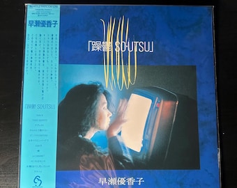 May include: A blue vinyl record with a woman looking at a television screen. The album cover features the text "躁鬱 SO-UTSU" and "早瀬優香子".