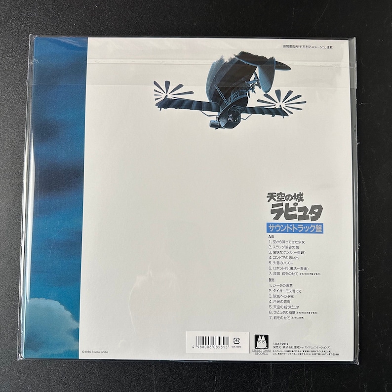 May include: The back of a vinyl record album cover for the soundtrack to the animated film "Castle in the Sky" (known as "Laputa: Castle in the Sky" in Japan). The cover features a white background with a blue sky and clouds at the bottom. The album title is in Japanese and English, and the track list is printed in Japanese. The album cover also includes a barcode and copyright information.