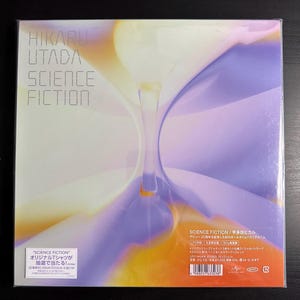 May include: A pink and yellow vinyl record cover with the title "Science Fiction" by Hikaru Utada. The cover features a swirling, abstract design with a light blue hourglass shape in the center.