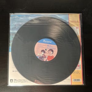 K&ouml;nnte beinhalten: Schwarze Vinyl-Schallplatte in einer transparenten Plastikh&uuml;lle. Das Album hat ein blau-wei&szlig;es Etikett mit japanischem Text und Cartoon-Illustrationen. Das Albumcover enth&auml;lt ebenfalls japanischen Text.