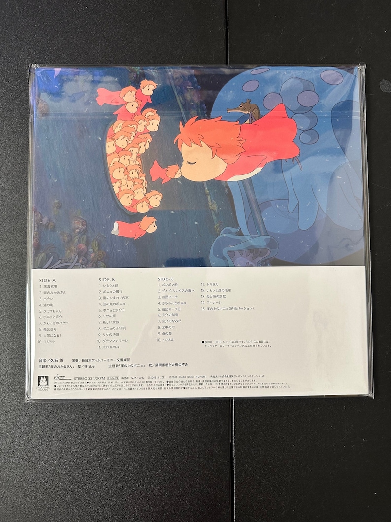 May include: A vinyl record album cover featuring a colourful illustration of a young girl with red hair and a red dress, swimming with a large, blue, jellyfish-like creature. The album is titled "Ponyo" and features the names of the composer, conductor, and singer. The album cover also includes a track list for each side of the record.