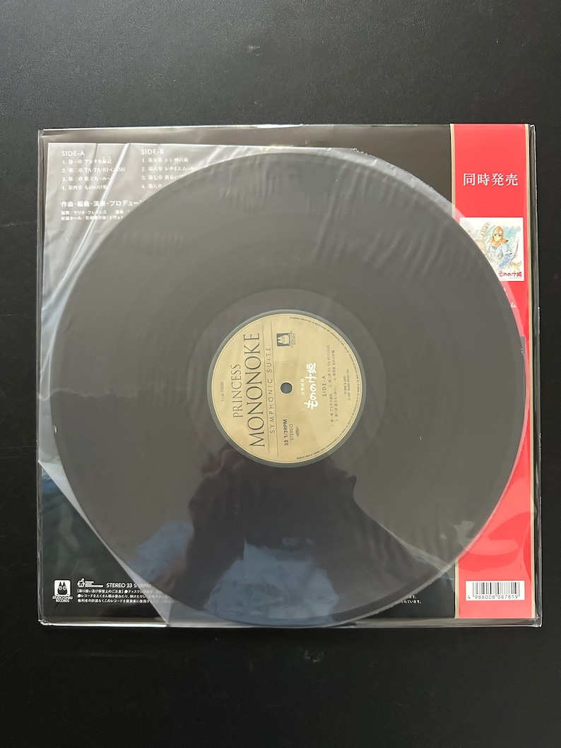 May include: A black vinyl record with a white label that says "Princess Mononoke Symphonic Suite" and "もののけ姫". The record is in a clear plastic sleeve with a red and white label that says "Simultaneous Release".