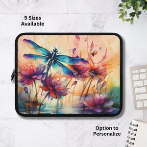 May include: A laptop sleeve with a colorful watercolor design featuring a blue dragonfly and pink flowers. The background is a soft yellow with a hint of orange. The sleeve has a zipper closure.