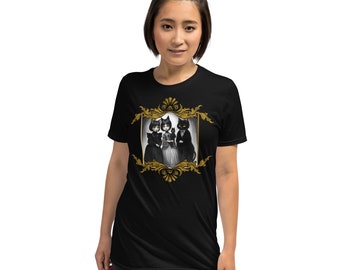 May include: Black t-shirt with a gold-framed illustration of three black cats in Victorian attire. The cats are depicted in a stylized manner. The frame has intricate gold detailing. The t-shirt is made of a soft fabric.