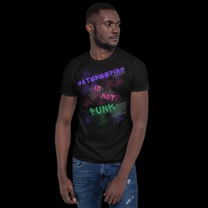 May include: Black t-shirt with the text "GATEKEEPING is NOT PUNK" in a graffiti-style design. The text is in purple, pink, and green, with a splatter effect. The shirt is worn by a person.