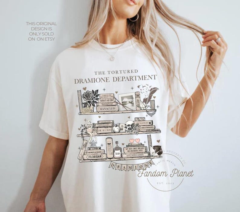 May include: White t-shirt with a graphic of a bookshelf with books, potions, and other items. The text "The Tortured Dramione Department" is above the bookshelf. The text "Fandom Planet" is below the bookshelf.