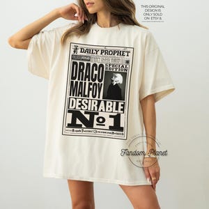 May include: A white t-shirt with a black and white graphic print of a newspaper headline that reads "Daily Prophet" and "Draco Malfoy Desirable No. 1".