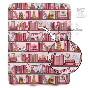 May include: A pink blanket with a detailed illustration of bookshelves filled with books, decorative items, and a banner. The books are in shades of pink and red. The text "THIS ORIGINAL DESIGN IS ONLY SOLD ON ETSY" is visible.