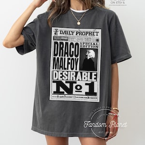 May include: A gray t-shirt with a black and white graphic print of the Daily Prophet newspaper featuring the headline "Draco Malfoy Desirable No. 1".