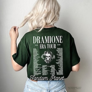 May include: A dark green t-shirt with a white graphic print of a skull with flowers and the text "DRAMIONE ERA TOUR EST 1879 EST 1980" and a list of song titles. The text "Fandom Planet" is printed below the graphic.
