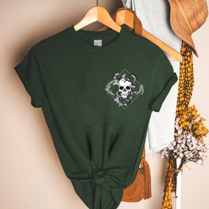 May include: A dark green t-shirt with a white graphic of a skull with a snake wrapped around it. The skull is surrounded by flowers and leaves.