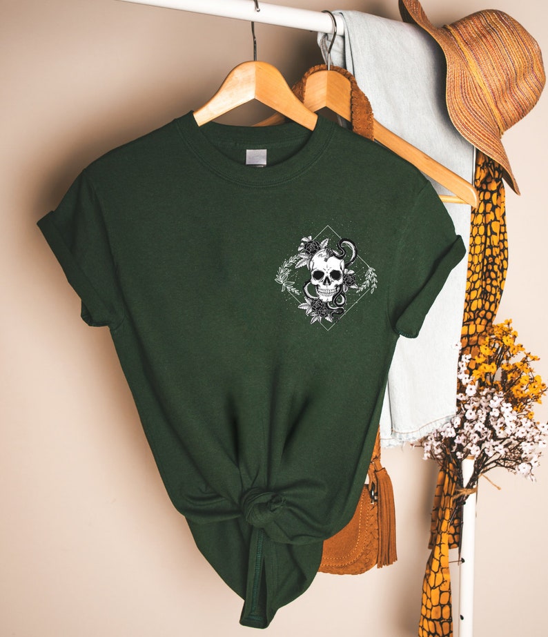 May include: A dark green t-shirt with a white graphic of a skull with a snake wrapped around it. The skull is surrounded by flowers and leaves.