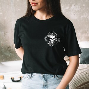 May include: Black t-shirt with a white graphic of a skull with a snake wrapped around it, surrounded by flowers. The graphic is in a diamond shape.