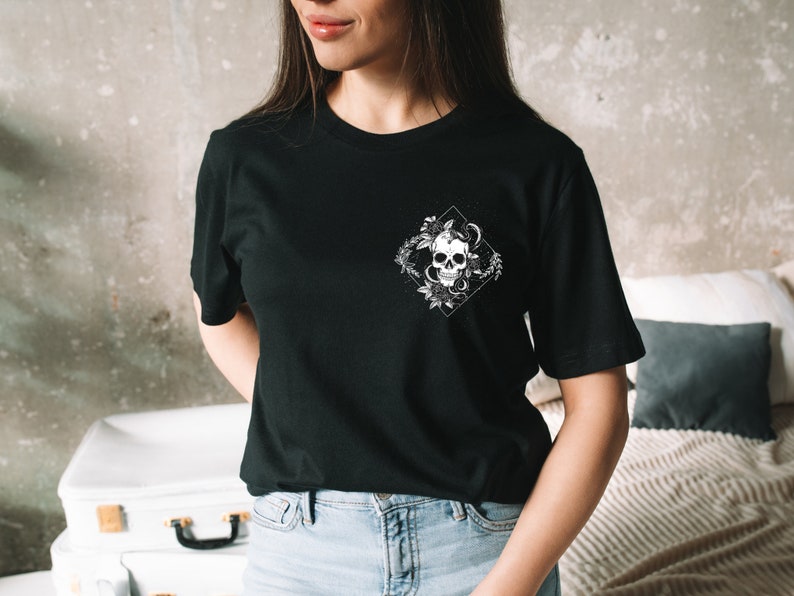 May include: Black t-shirt with a white graphic of a skull with a snake wrapped around it, surrounded by flowers. The graphic is in a diamond shape.