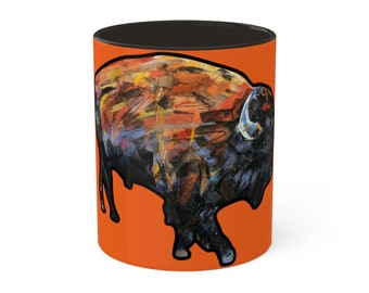 May include: Orange ceramic mug with a black interior and a colorful abstract painting of a bison on the front.