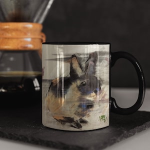 K&ouml;nnte beinhalten: Eine schwarze Kaffeetasse mit einem wei&szlig;en Design eines Kaninchens mit braunem und schwarzem Fell. Das Kaninchen schaut nach rechts und ist von einem aquarellartigen Hintergrund umgeben.