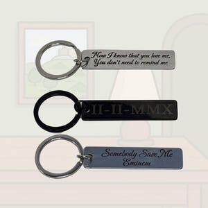 Pode incluir: Três chaveiros de metal com texto gravado. O chaveiro superior tem um anel prateado e uma etiqueta retangular com a inscrição "Now I know that you love me, You don't need to remind me." O chaveiro do meio é preto com "II-II-MMX" gravado.