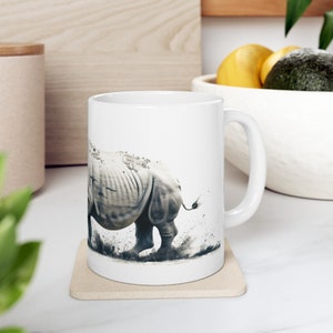Könnte beinhalten: Weiße Keramiktasse mit einer Schwarzweißillustration eines Nashorns, das durch Dreck rennt. Die Tasse hat einen Henkel auf der rechten Seite.