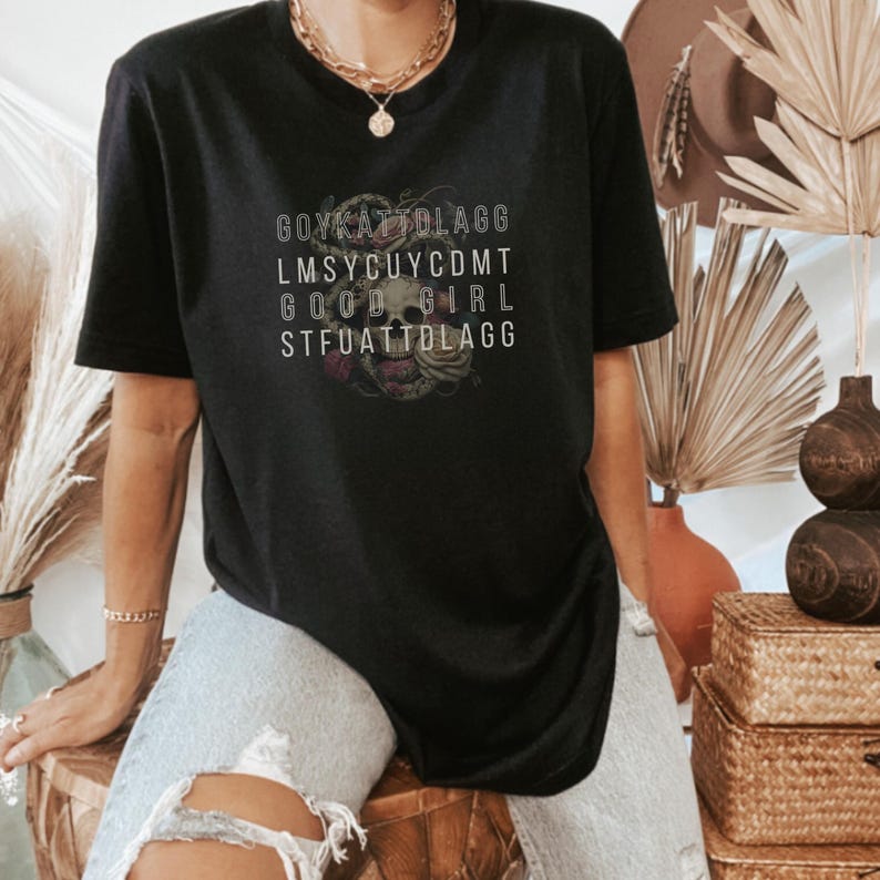 May include: Black t-shirt with a skull and roses graphic and the text "GOYKATZTOLAGG LMSYCUYCDMT GOOD GIRL STFUATTBLAGG"