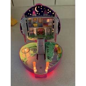 May include: A heart-shaped Polly Pocket playset that opens to reveal a multi-level castle interior with a night sky backdrop featuring a crescent moon and stars. The interior includes a throne room, a bedroom, a staircase, and a small figure.