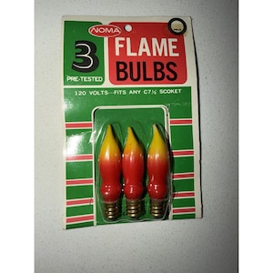 Pode incluir: Um pacote de três lâmpadas de chama Noma com acabamento degradê vermelho e amarelo. A embalagem é verde e branca com listras vermelhas, contendo o texto 3 FLAME BULBS, 120 VOLTS e FITS ANY C7 1/2 SOCKET. As lâmpadas têm bases de metal.