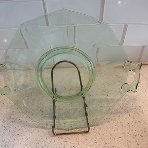 May include: A clear green glass serving dish with two handles. The dish has a scalloped edge and a raised center.