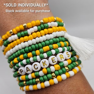 May include: A stack of green, white, and yellow beaded bracelets with gold accents. The bracelets spell out "PACKERS" in white beads with gold lettering. The text "*SOLD INDIVIDUALLY* Stack available for purchase" is at the top of the image.