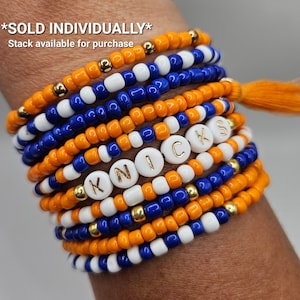 May include: A stack of orange, white, and blue beaded bracelets with gold accents. The bracelets spell out "KNICKS" with white letter beads. The text *SOLD INDIVIDUALLY* and *Stack available for purchase* is visible.