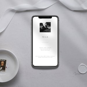 May include: A smartphone displays a wedding save-the-date card. The card features a black and white photo of a couple, the initials "N&A", and the text "Save the Date". A white ribbon, a bowl with a stamp, and a wax seal are also visible.