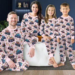 May include: A family of four wearing matching pink pajamas with a monster truck and Easter egg print. The pajamas have long sleeves and long pants.