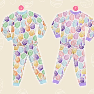 May include: Two sets of Easter pyjamas. One set has a light blue trim, and the other has a purple trim. Both sets feature a repeating pattern of colourful Easter eggs and bunnies on a white background. The pyjamas include a long-sleeved top and matching trousers.