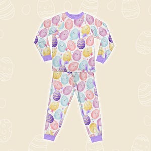 May include: A two-piece pajama set with a repeating pattern of pastel Easter eggs with faces and bunny ears. The long-sleeved top and trousers have purple trim and a drawstring waist. The pajamas are made of a soft, lightweight fabric.