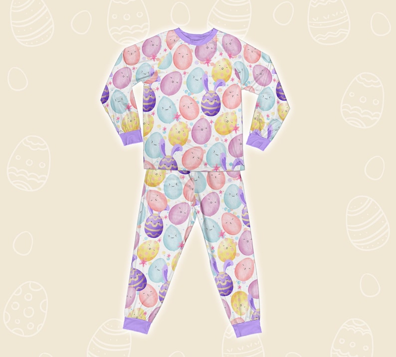 May include: A two-piece pajama set with a repeating pattern of pastel Easter eggs with faces and bunny ears. The long-sleeved top and trousers have purple trim and a drawstring waist. The pajamas are made of a soft, lightweight fabric.
